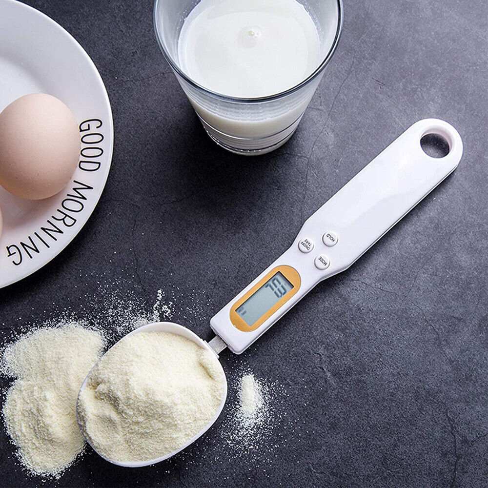 Digital Scale Spoon in white plastic with an orange-trimmed LCD display, holding a scoop of pale powder.