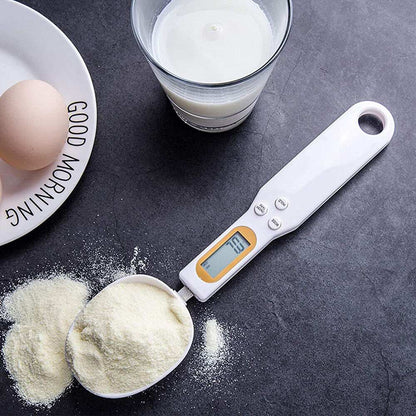 Digital Scale Spoon in white plastic with an orange-trimmed LCD display, holding a scoop of pale powder.